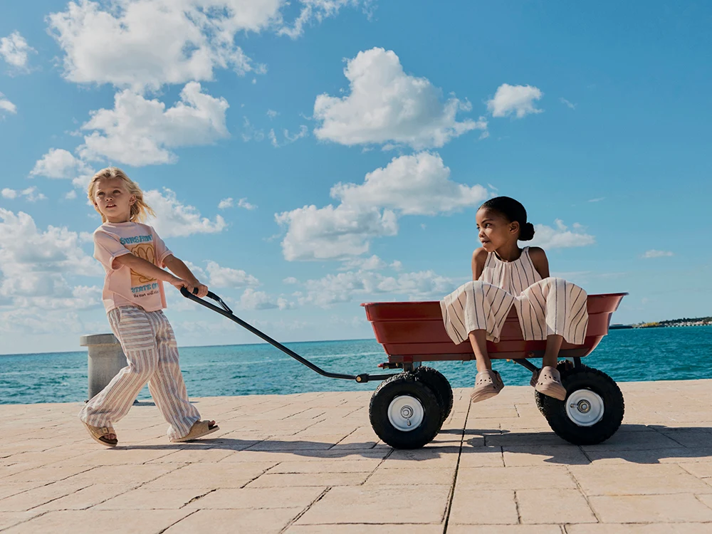 Two children wearing summer clothes playing with a push cart