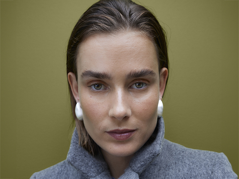 Woman wearing oversized silver earrings and a grey coat