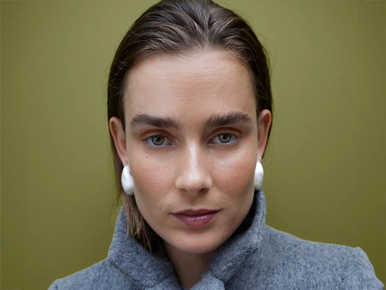 Woman wearing oversized silver earrings and a grey coat