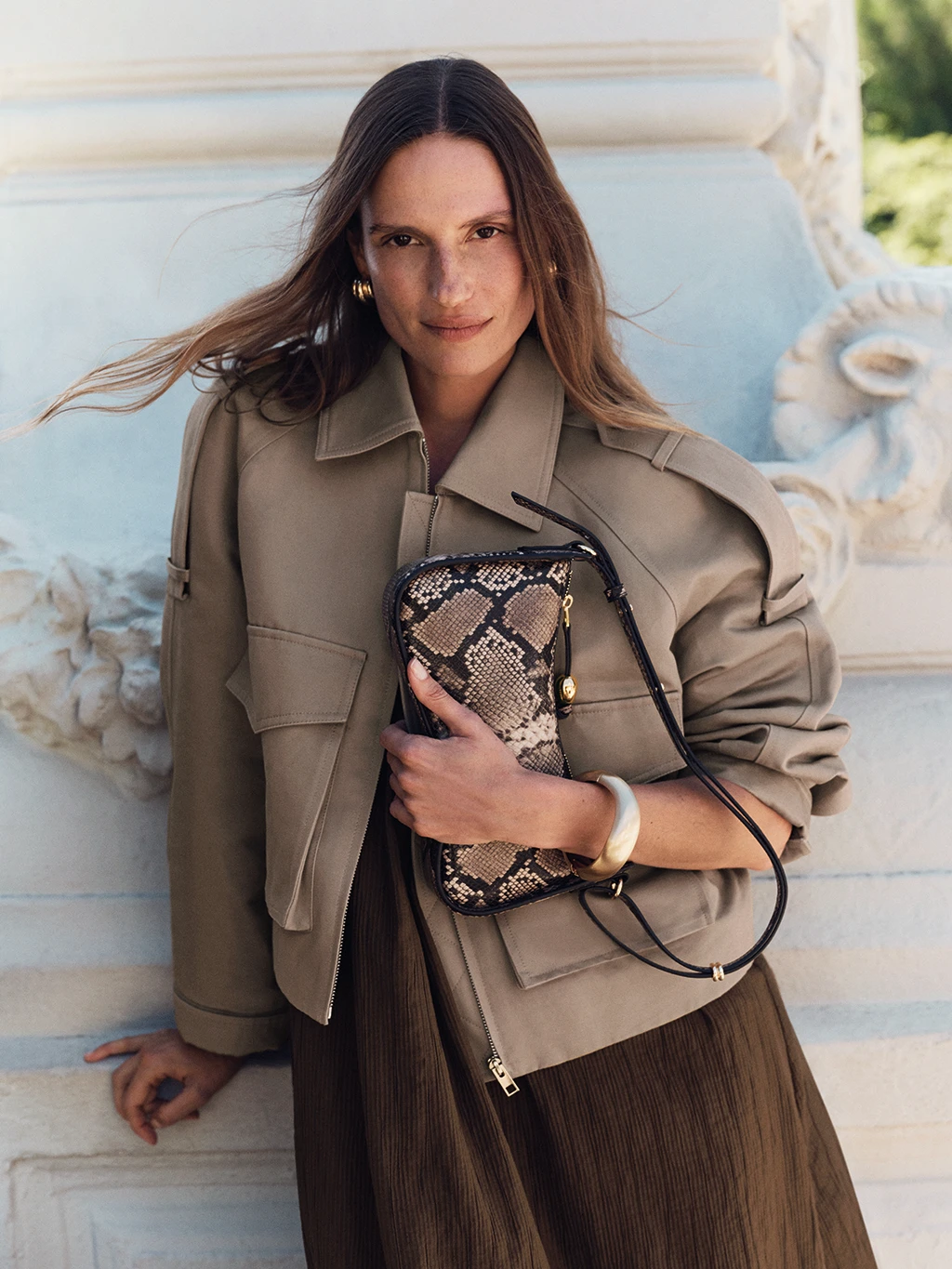 Woman wearing brown jacket and holding snake-print bag