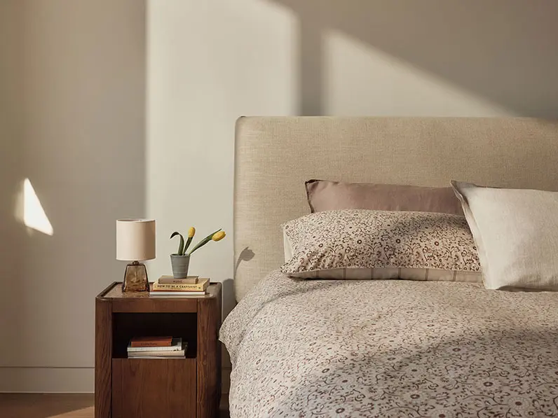 Serene bed setup with floral bedding and a glass lamp on a wooden bedside table