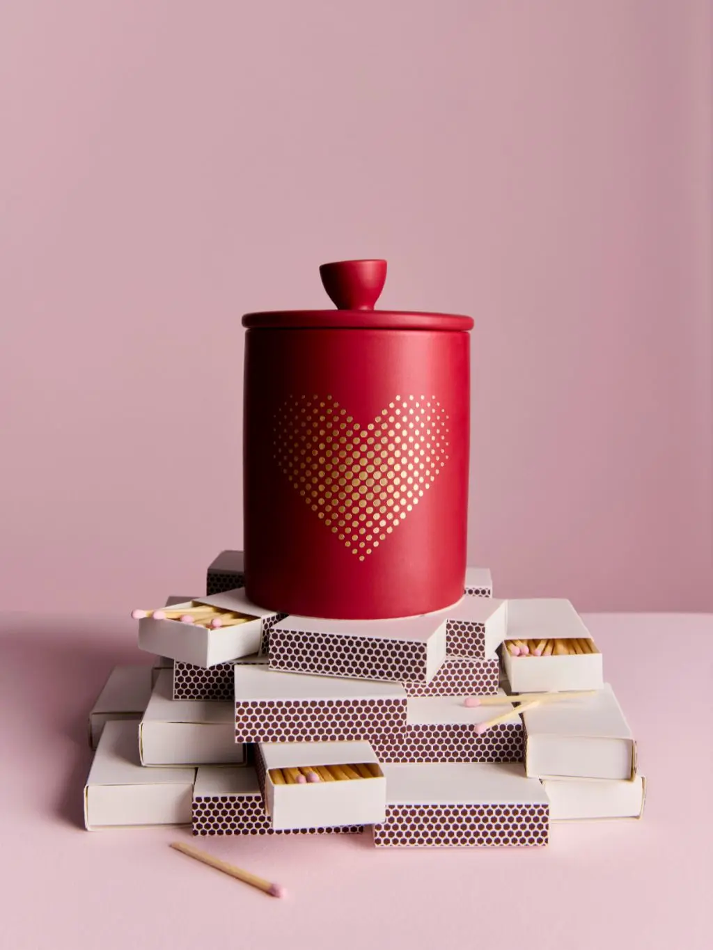 A red candle with a gold heart on it balanced on match boxes