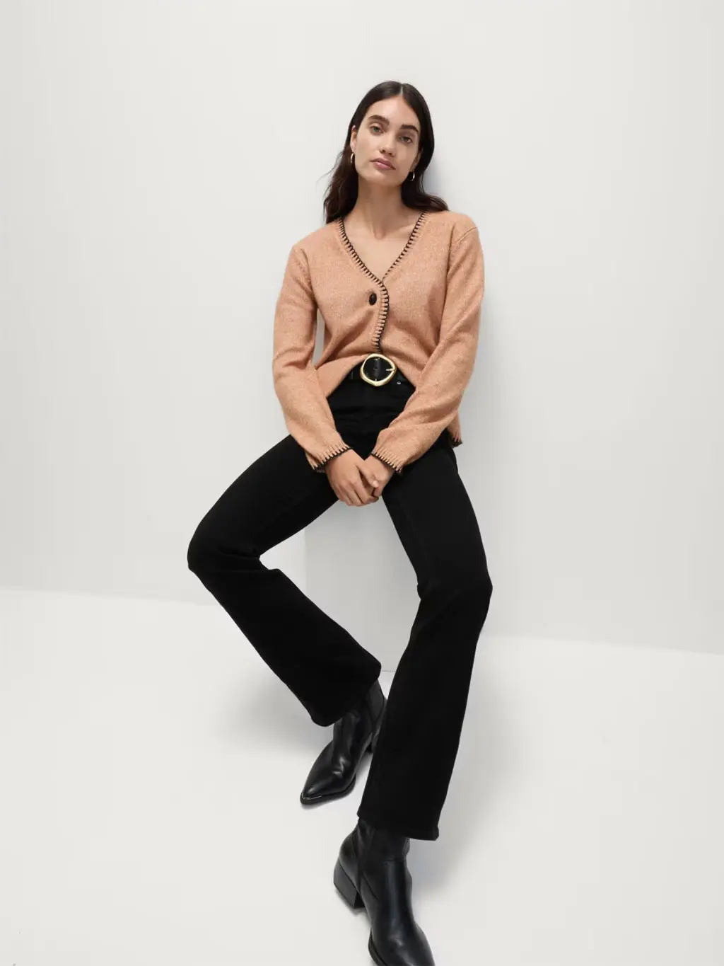Woman wearing black bootcut jeans, a peach cardigan, black belt and black cowboy boots.