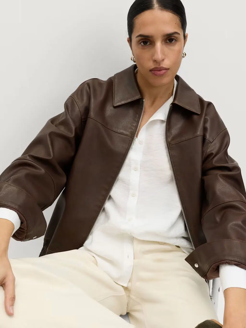 Woman wearing cream jeans with a white shirt and a brown leather jacket
