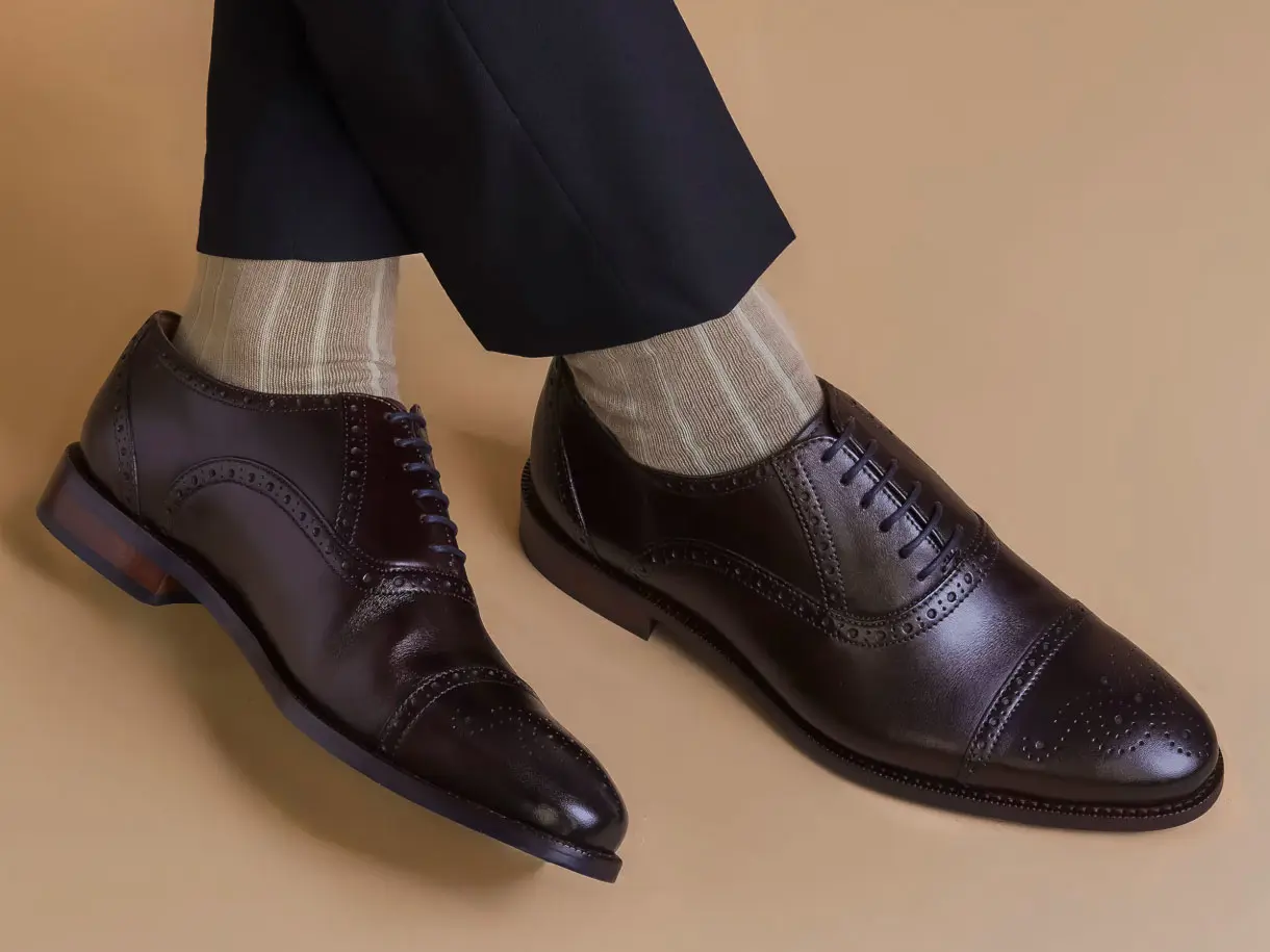 Man wearing dark brown brogues, beige striped socks and smart trousers