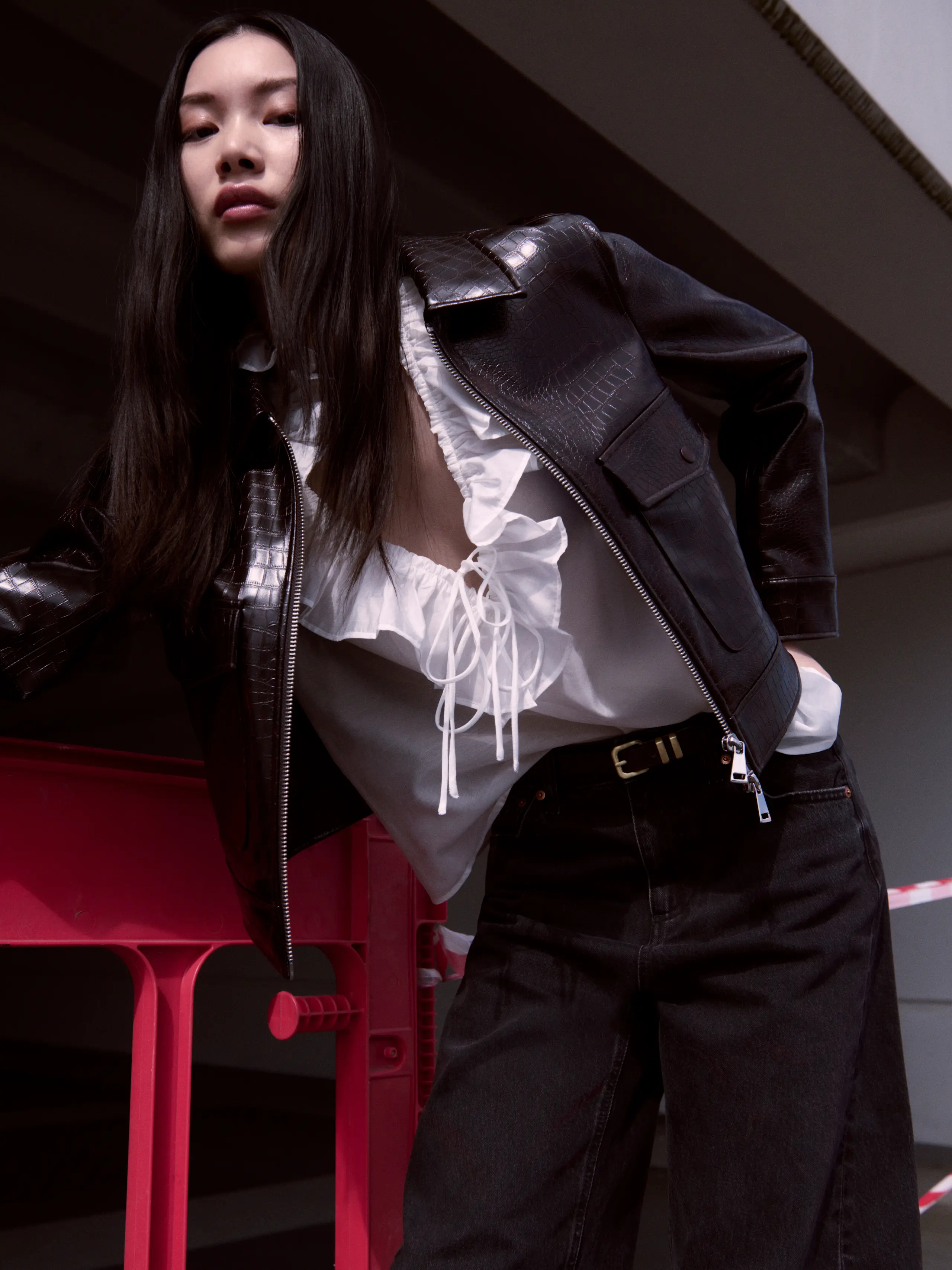 Woman wearing white ruffled blouse under black leather jacket and black jeans 