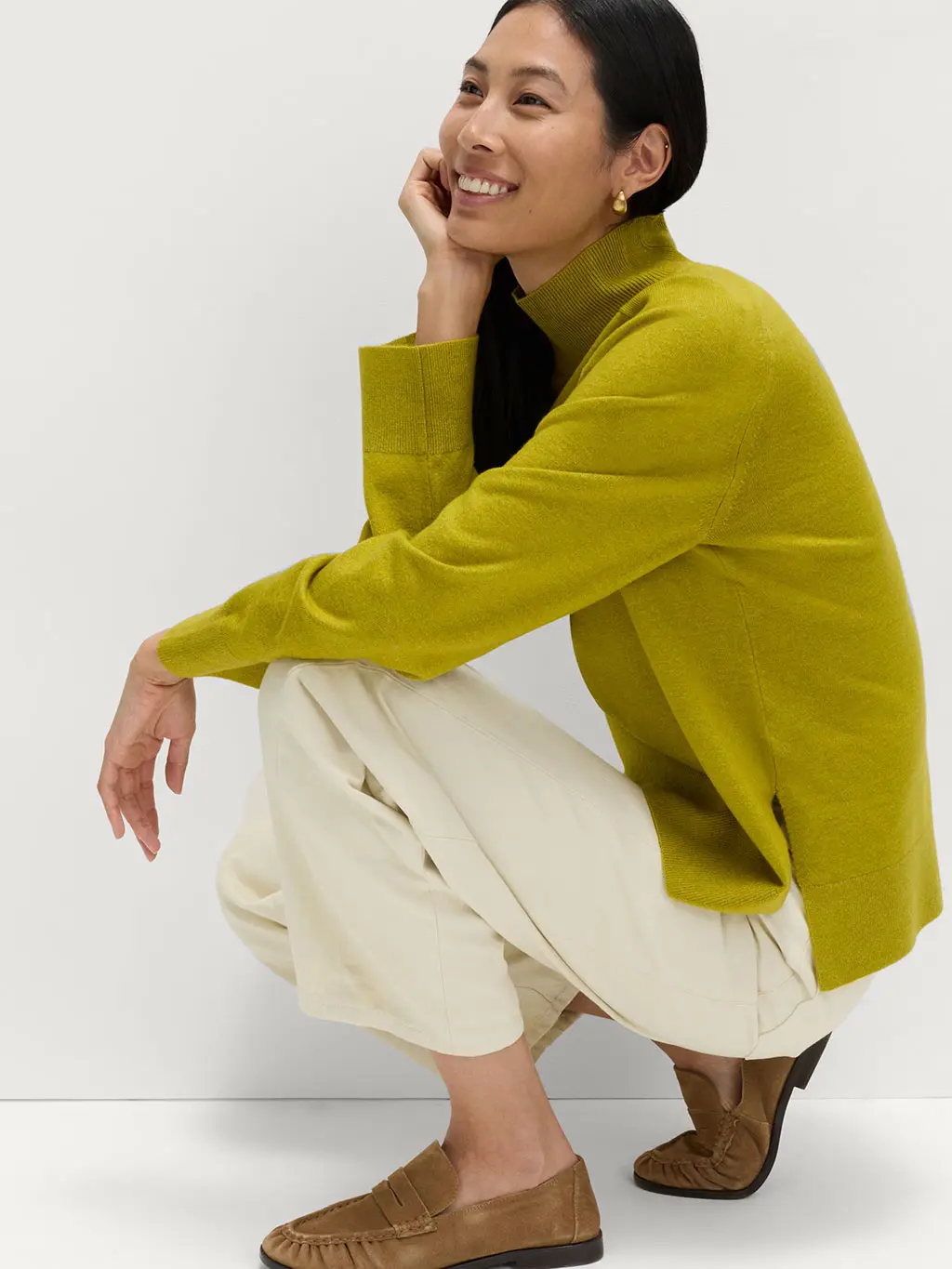 Woman wearing a moss funnel-neck jumper with cream trousers and loafers