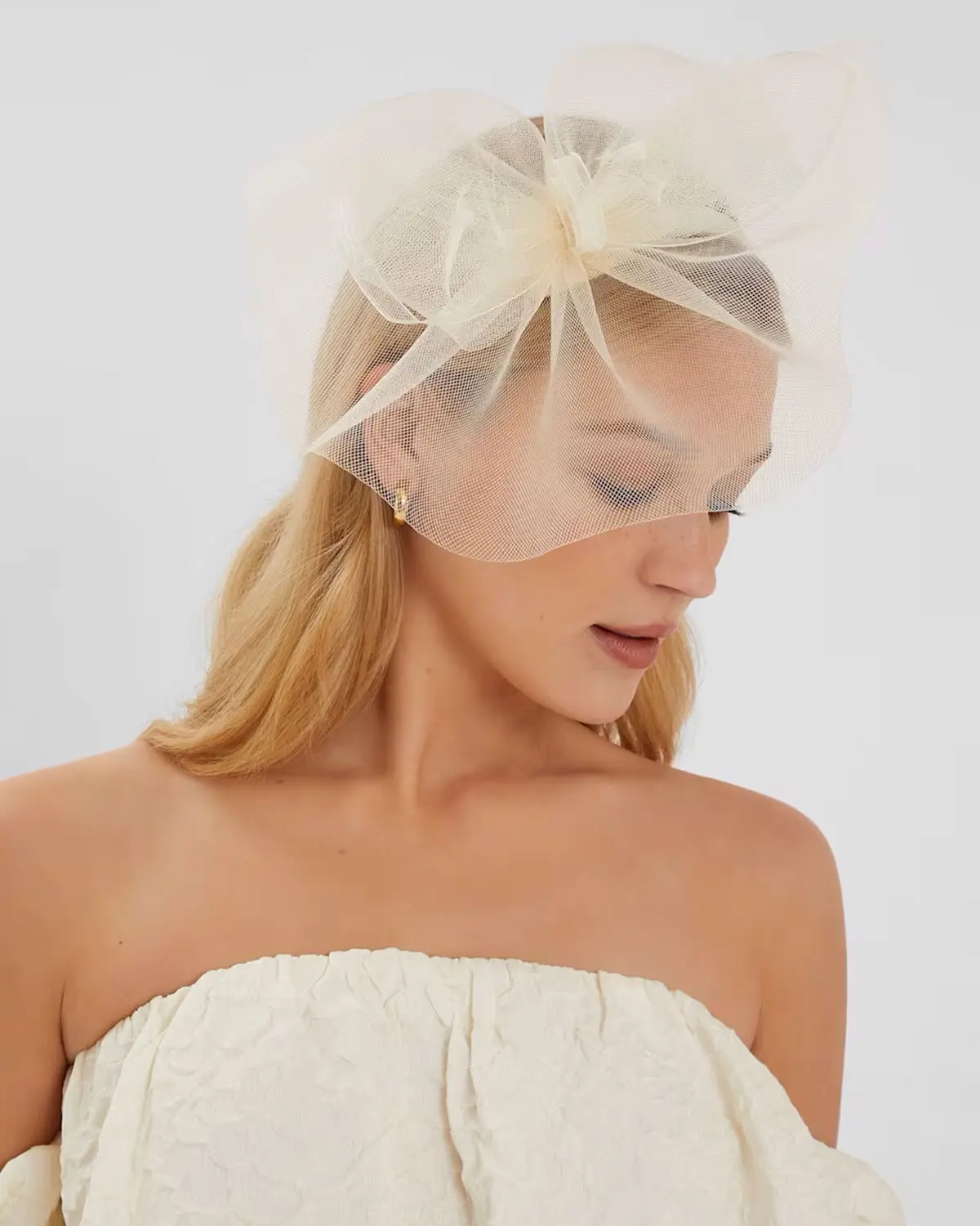 Woman wearing cream tulle fascinator with strapless cream dress and gold earrings