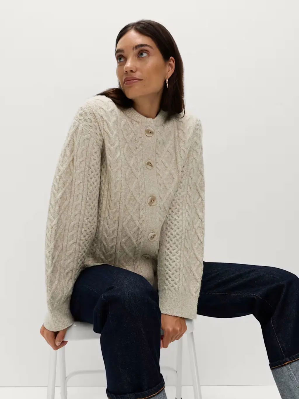 Woman wearing a cable-knit cardigan with indigo-blue jeans and silver earrings