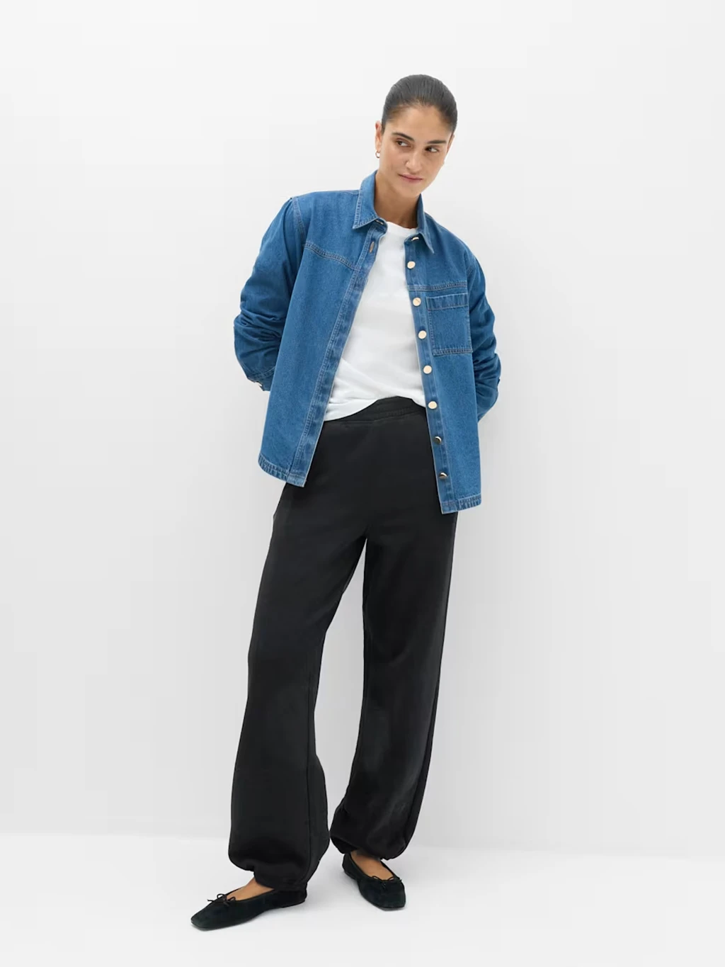 Woman wearing a pair of black joggers with a white T-shirt and blue denim shirt.