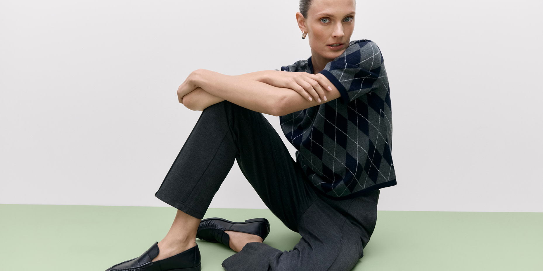 Woman wearing dark argyle-printed top, black trousers and black loafers