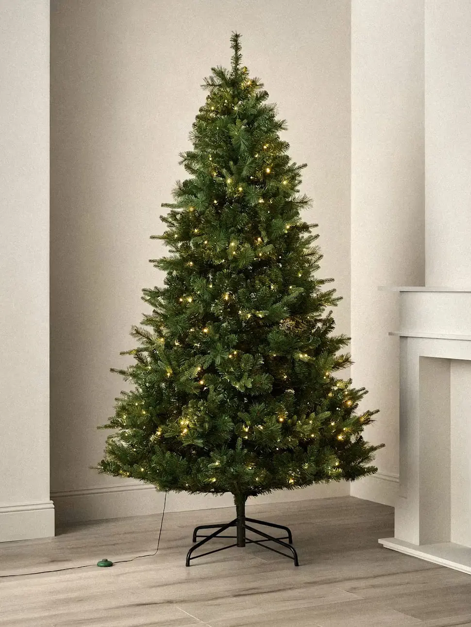 Tall artificial Christmas tree with warm white lights and metal stand.