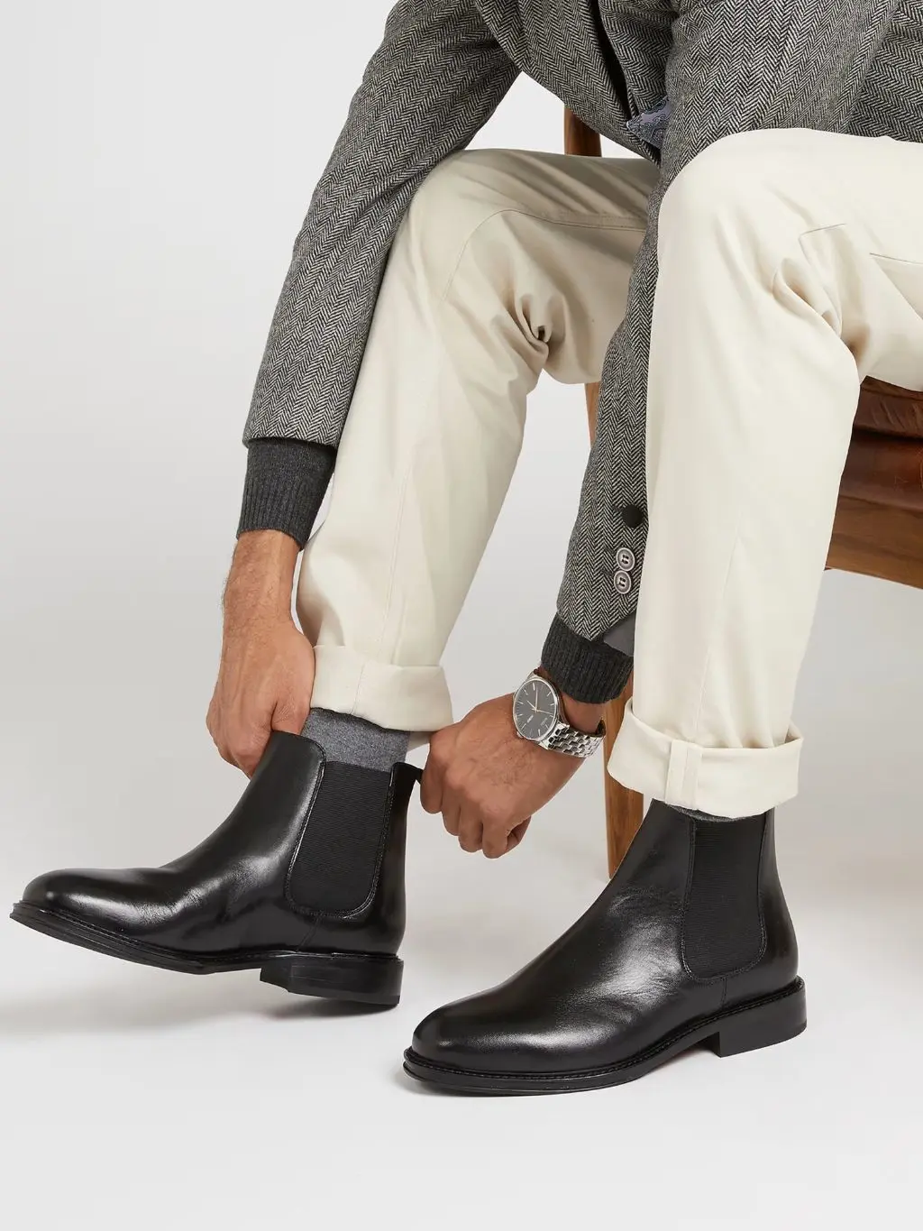 A man reaching down to pull on his black Chelsea boots with grey socks
