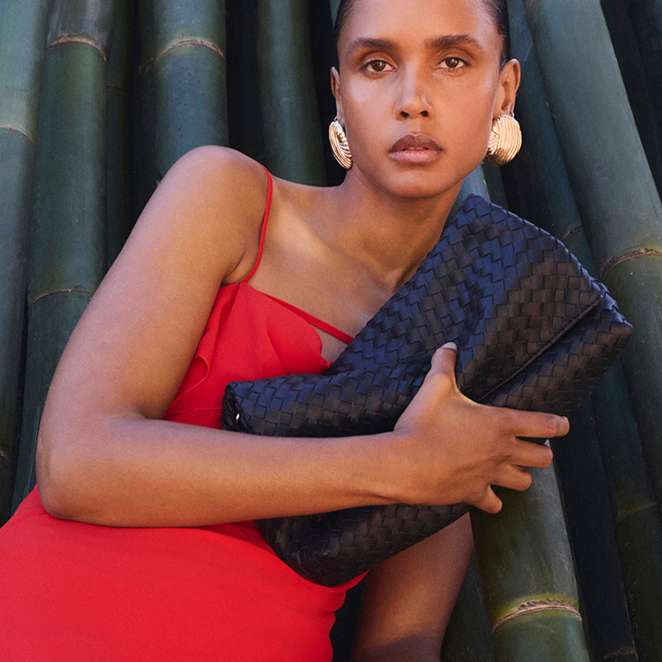 Woman wearing red dress, black woven clutch bag and gold jewellery