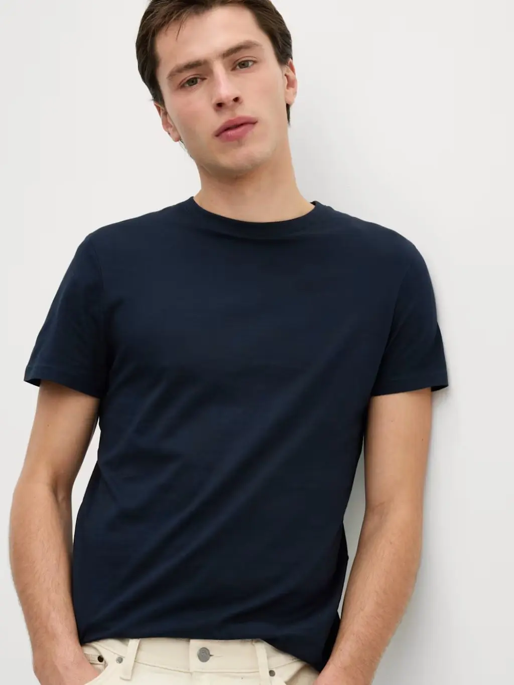 A man wears a slim fitting black tshirt with cream jeans