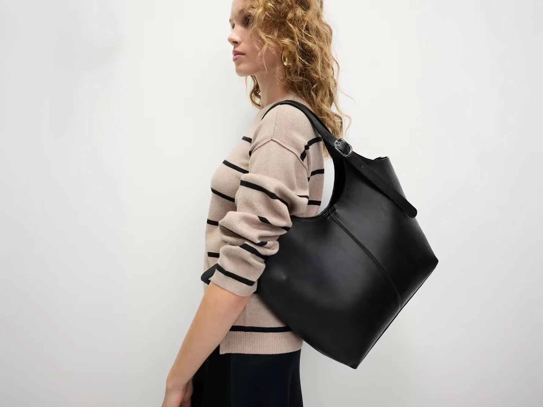 Woman wearing striped jumper and black trousers with a black tote bag.