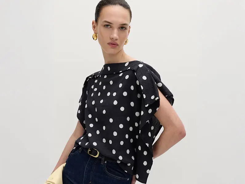 Woman wearing a polka-dot blouse with indigo jeans, gold jewellery, a black belt and a yellow clutch bag