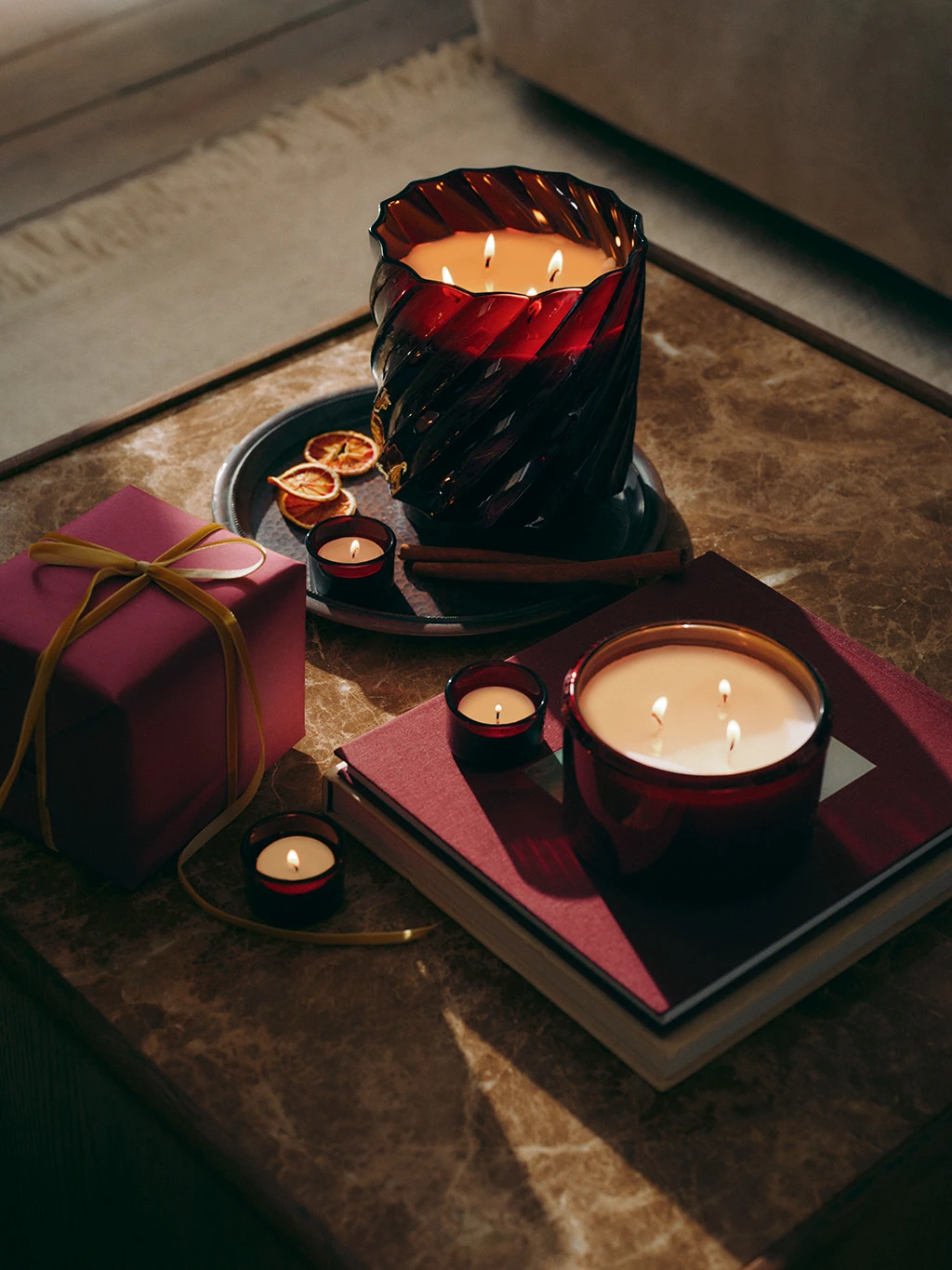 Two large M&S candles on a marble table, surrounded by a red present and mini candles.
