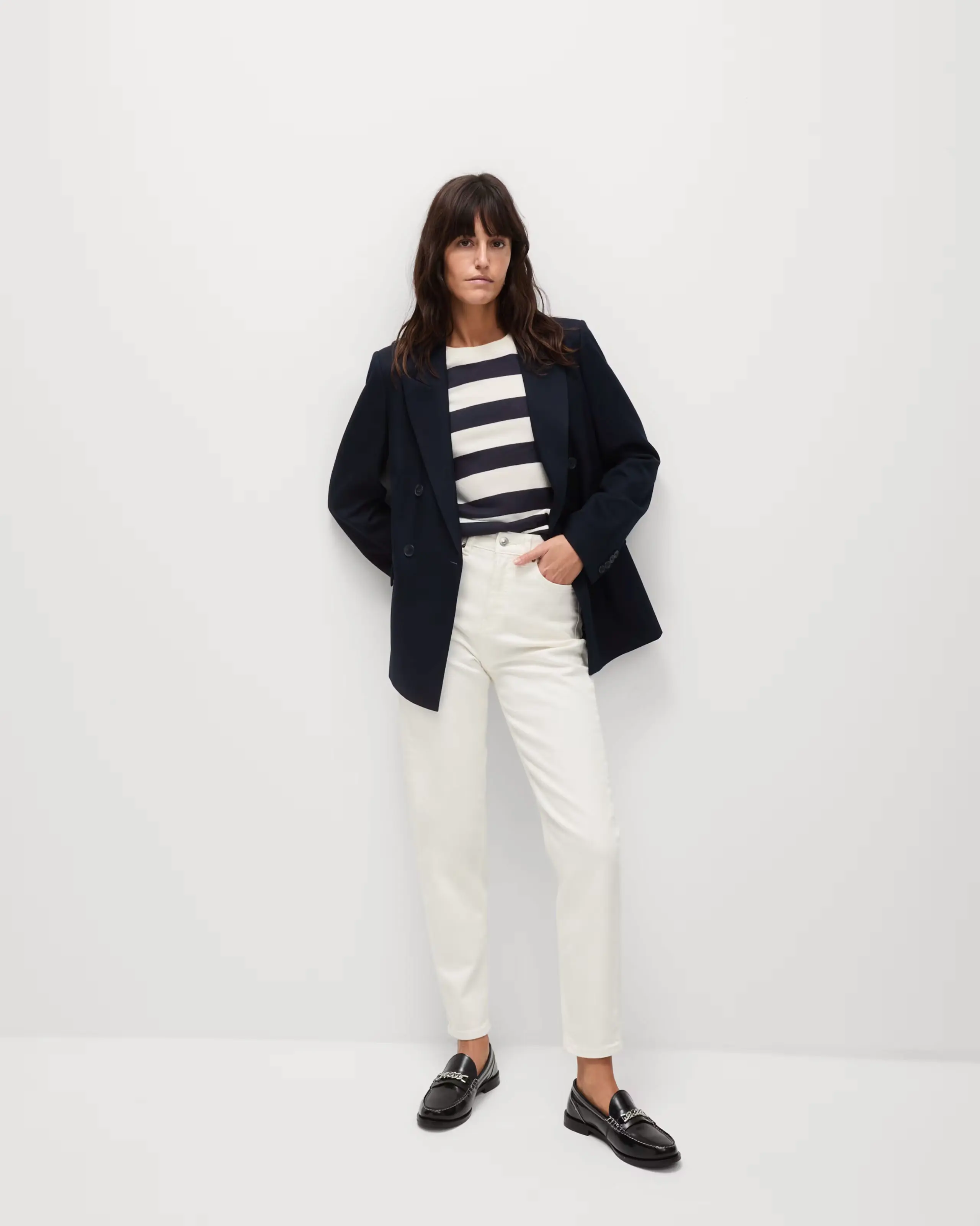 Woman wearing white mom jeans with a striped top, black blazer and loafers.
