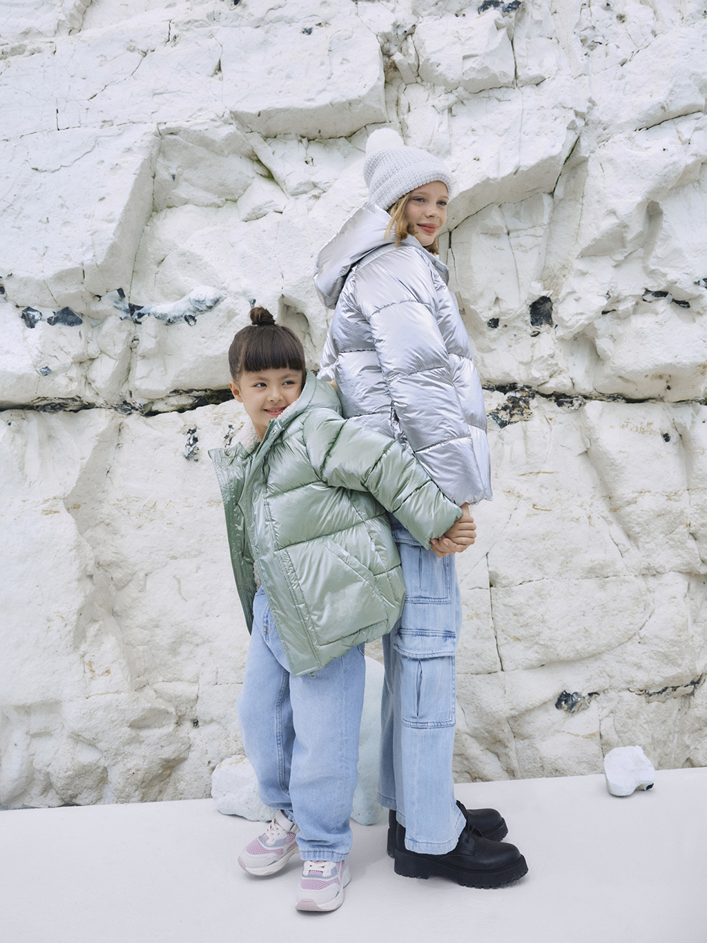 Girls wearing pastel padded raincoats by cliffs at the beach