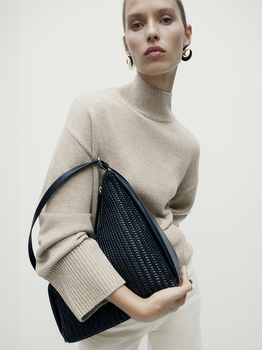 Woman wearing oatmeal funnel neck jumper holding a black handbag