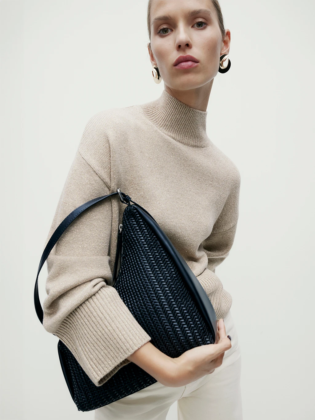 Woman wearing oatmeal funnel neck jumper holding a black handbag