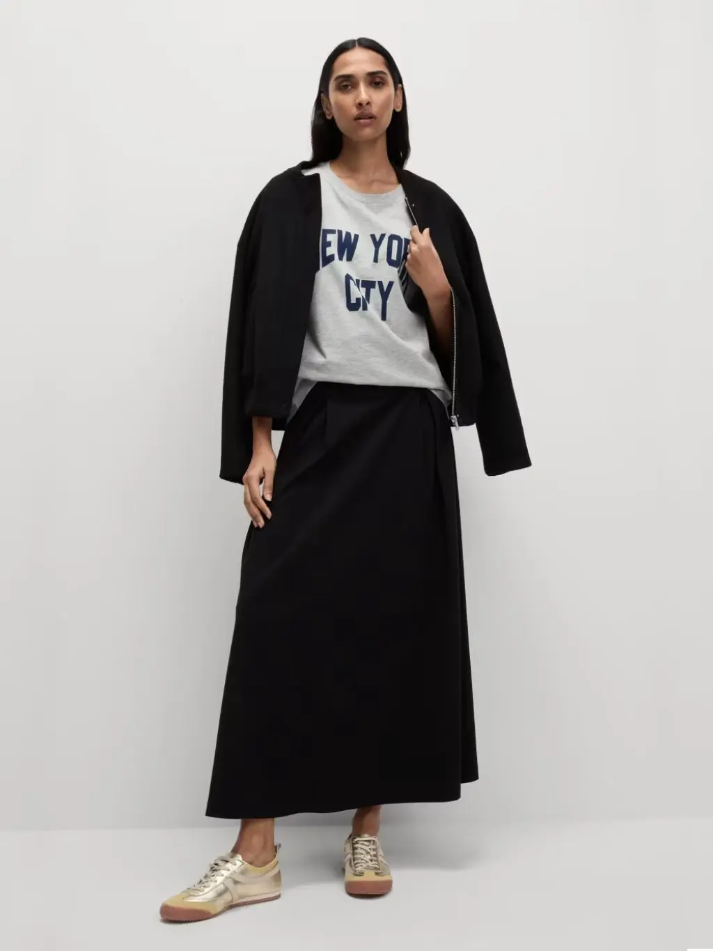 A woman wears an oversized graphic t-shirt tucked into a midi skirt with a blazer thrown over her shoulders