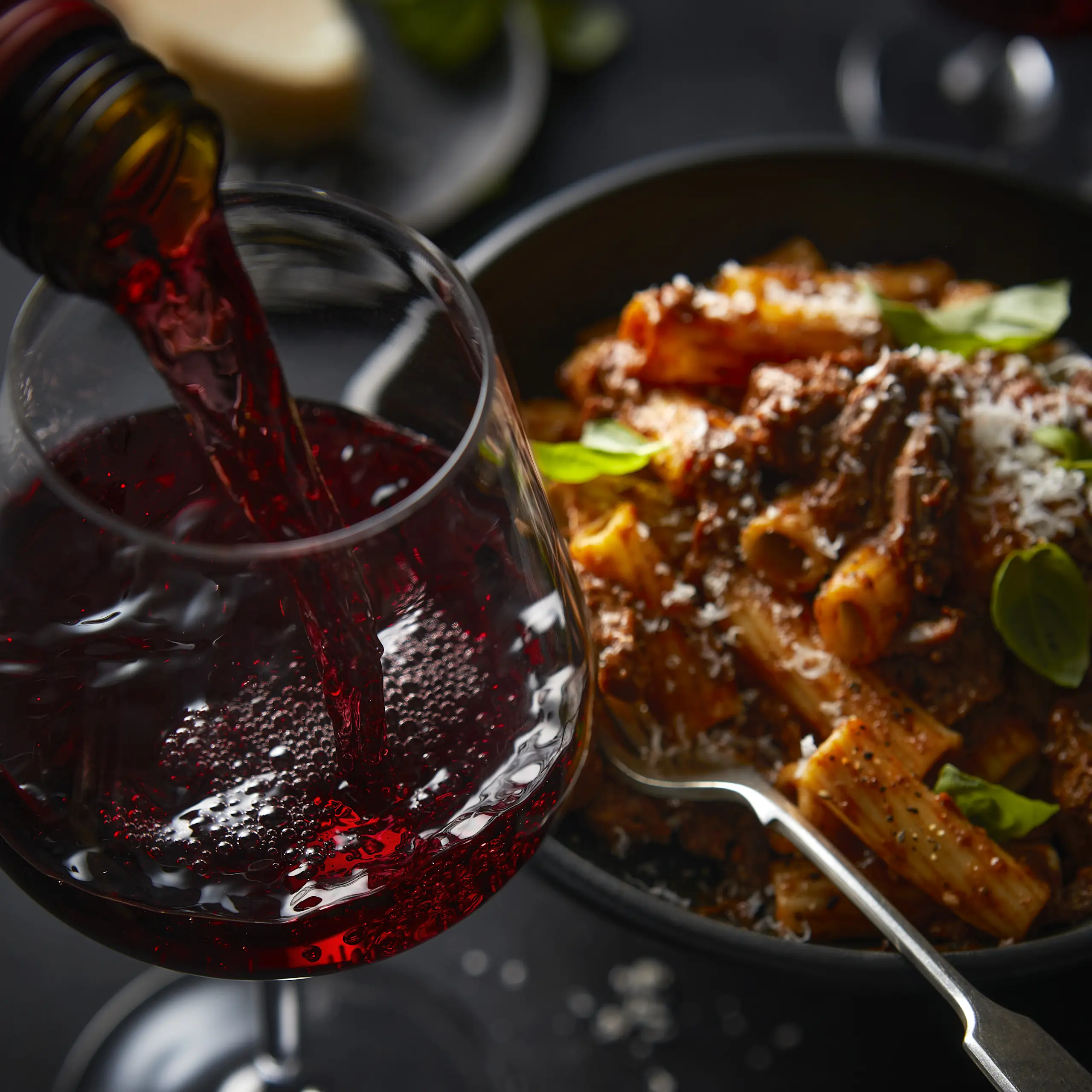 Glass of red wine being poured with bowl of pasta