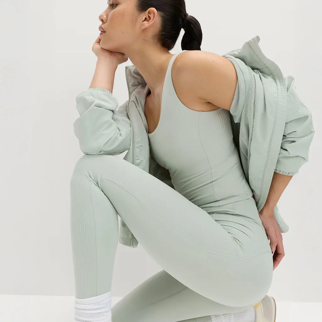 Woman stretching whilst wearing a light green sports bra and leggings with a matching jacket