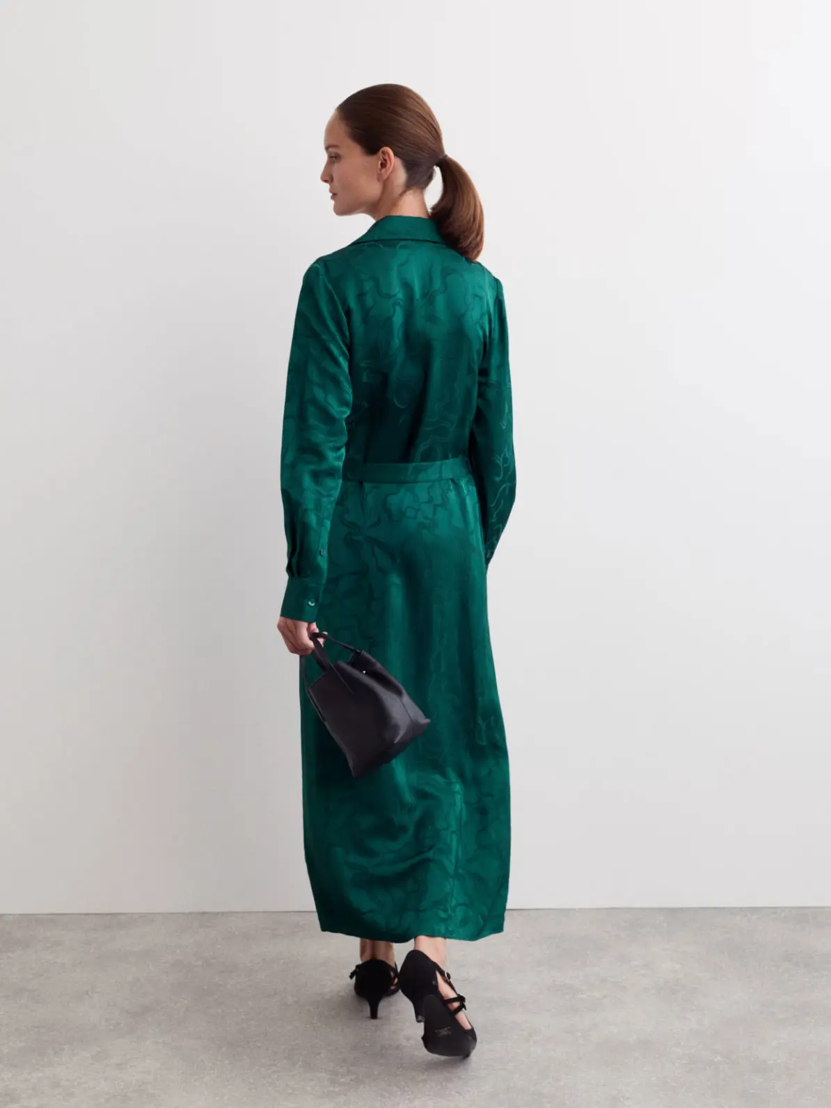 Woman wearing emerald green dress with black kitten heels and black bag 