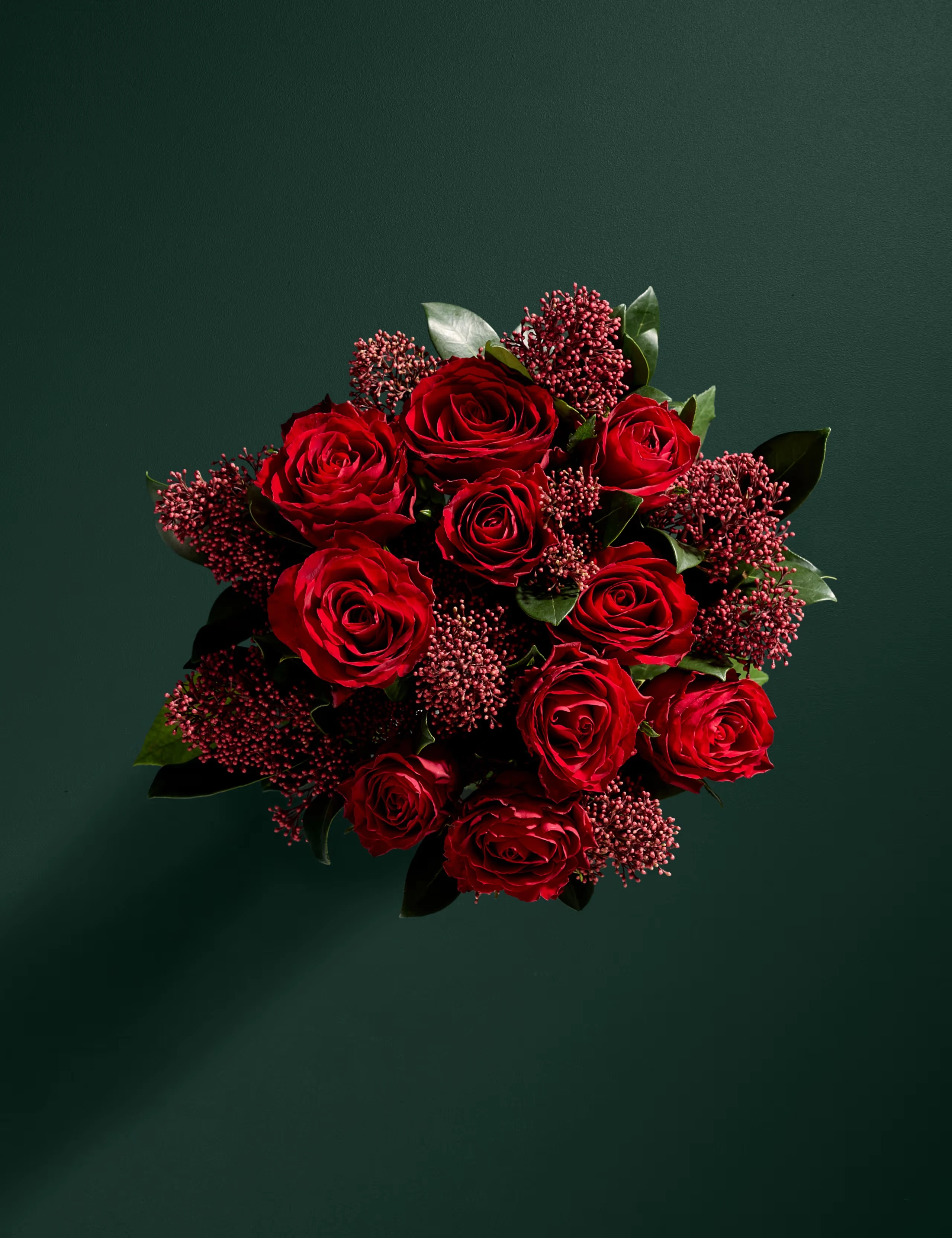 Bouquet of red roses with seasonal green foliage and berries.
