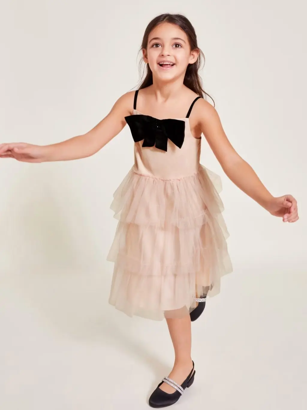 A girl in a pale pink tiered black tie event dress with a black bow