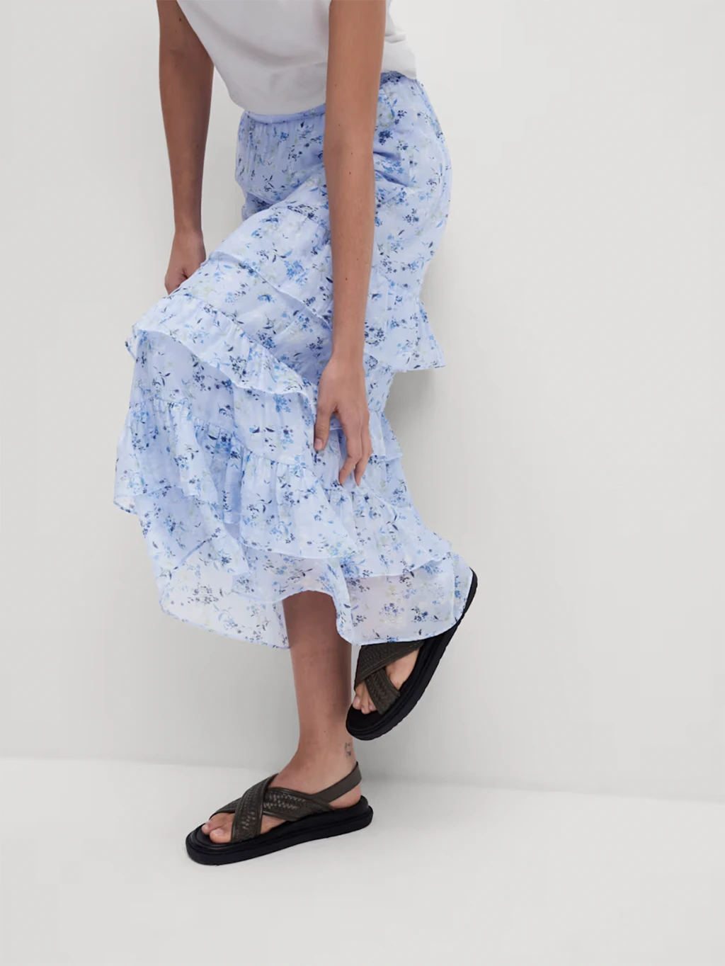 woman wearing blue printed skirt, a white top and black sandals