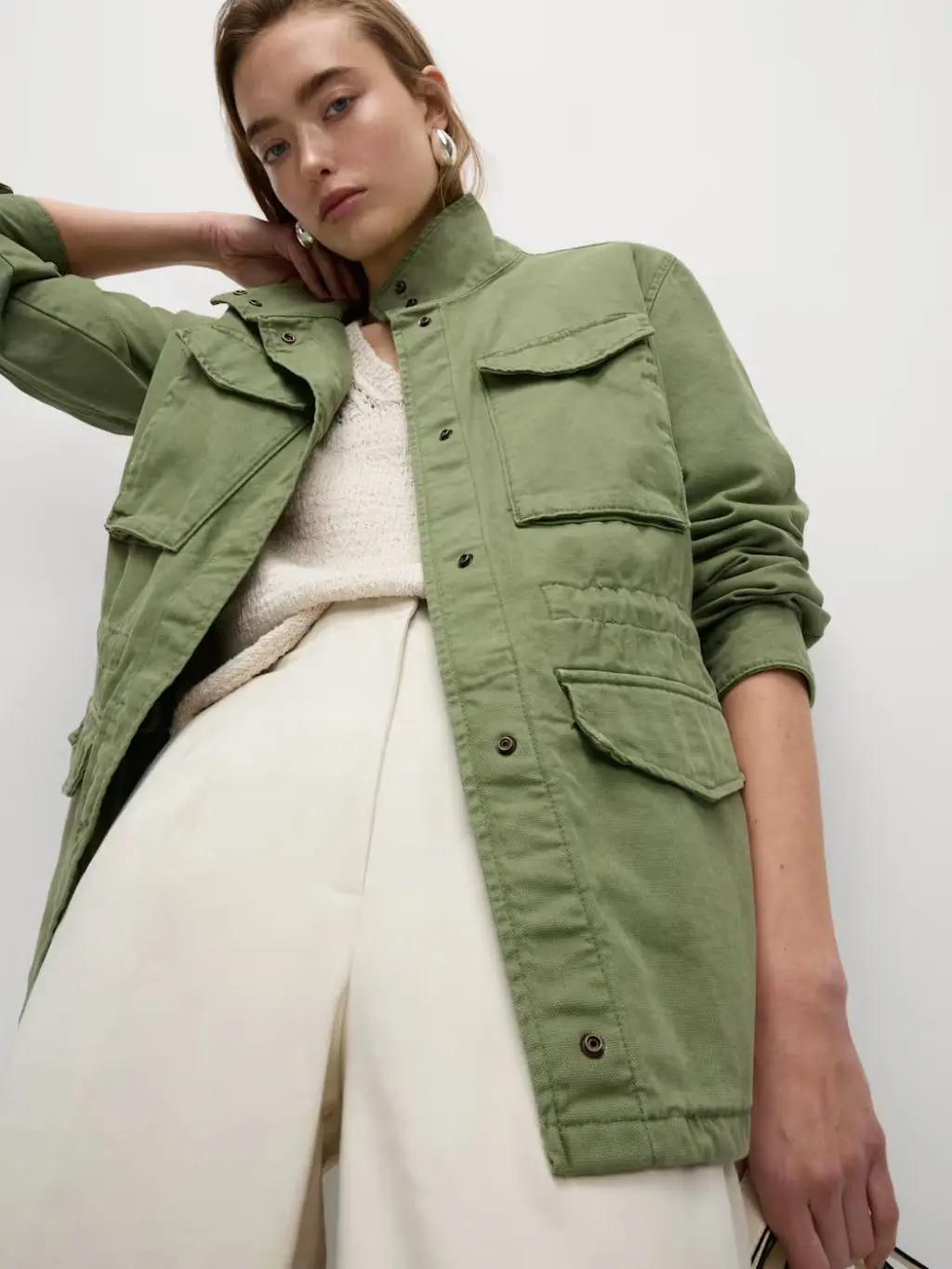 A woman wears a khaki utility jacket over crea