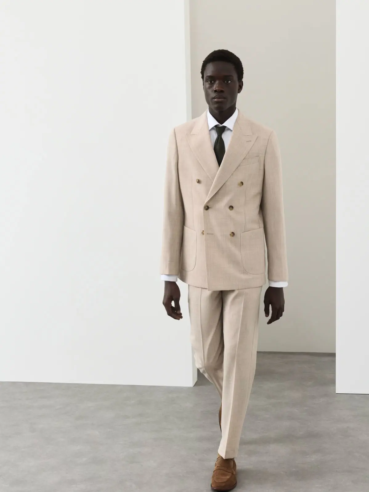 Man wearing light-toned suit with a white shirt, black tie and suede loafers