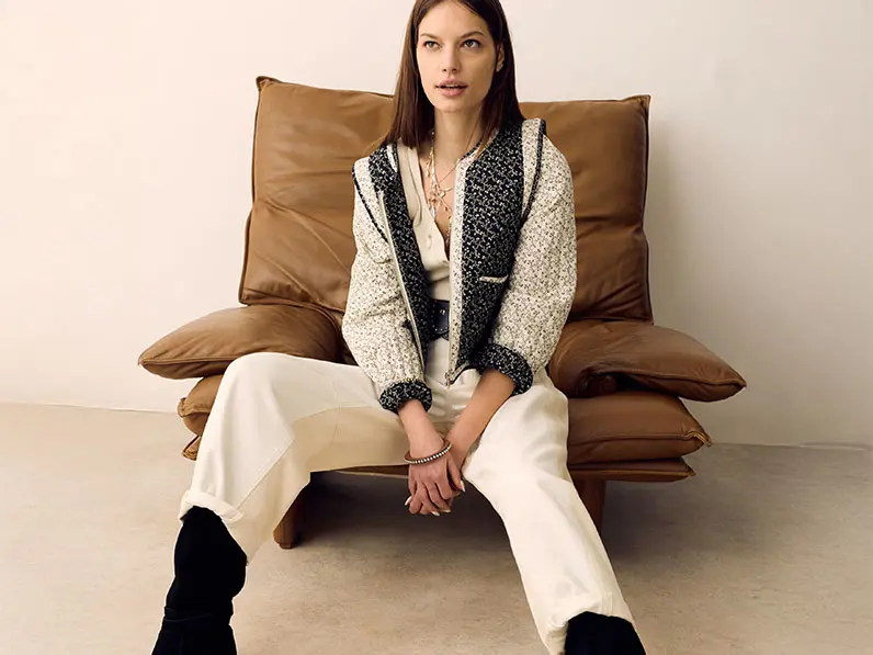 Woman wearing a quilted jacket with a cream blouse, white jeans and slouchy black boots