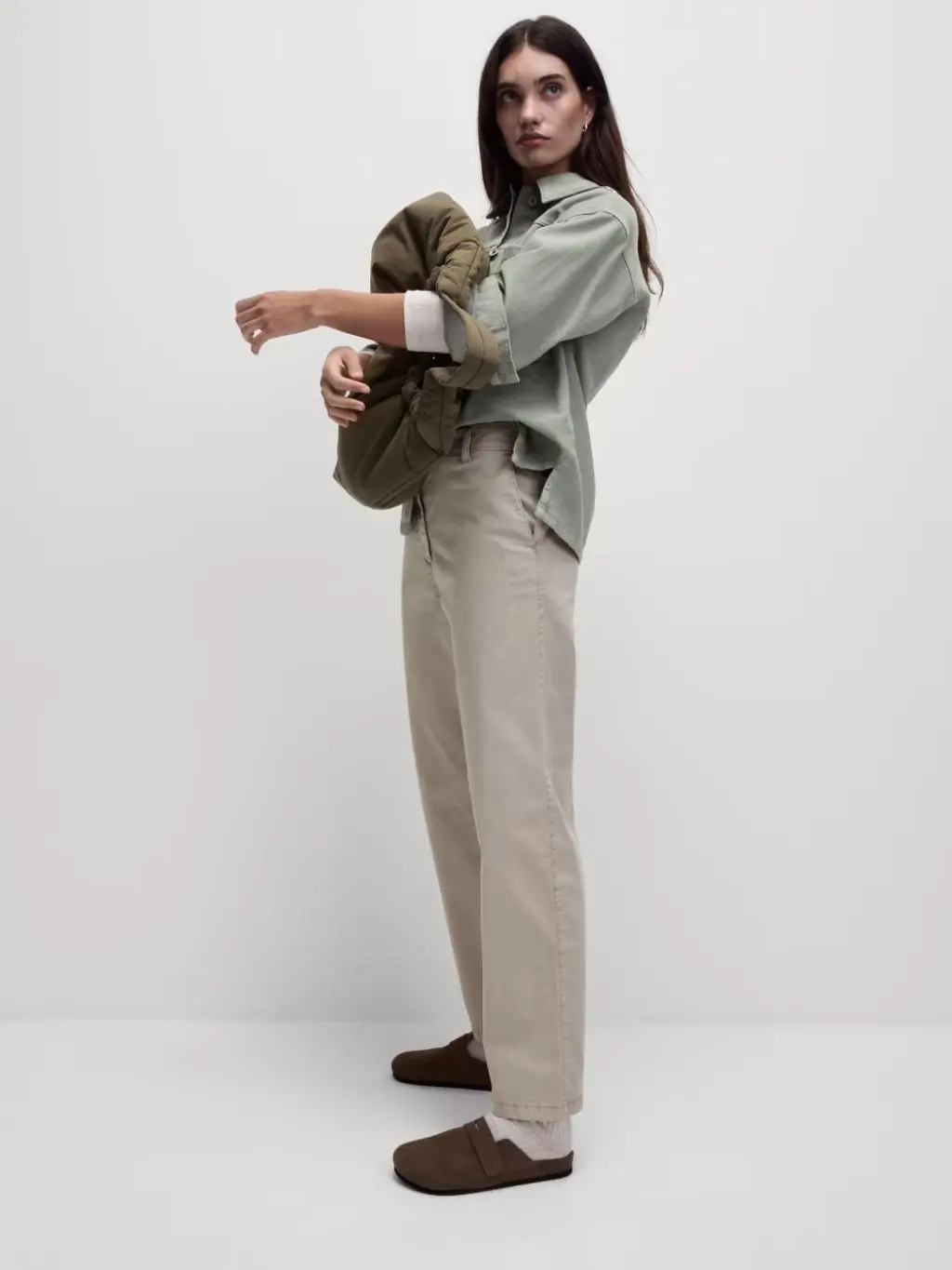 A woman wears chinos, a t-shirt, jacket and slilp on clogs