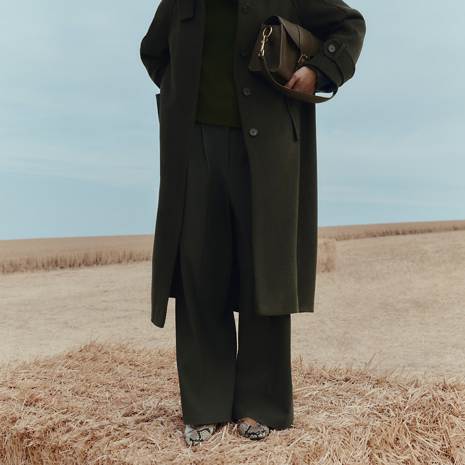 Woman wearing khaki coat, jumper and trousers in a field