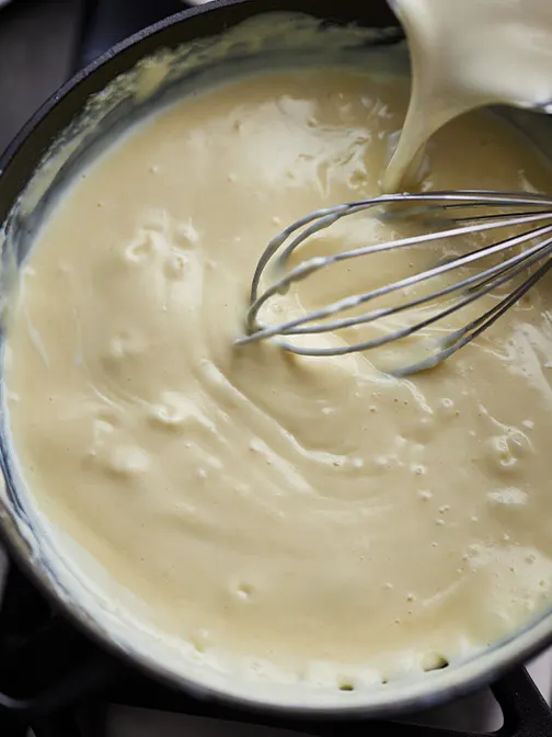 Whisking creamy roux while adding milk