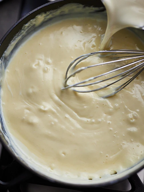 Whisking creamy roux while adding milk