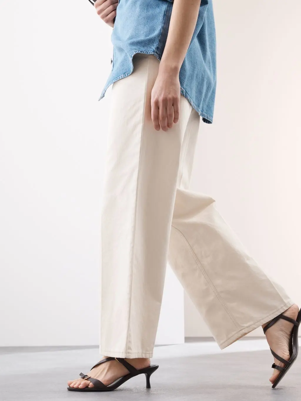Woman wearing loose cream summer jeans and black heeled sandals