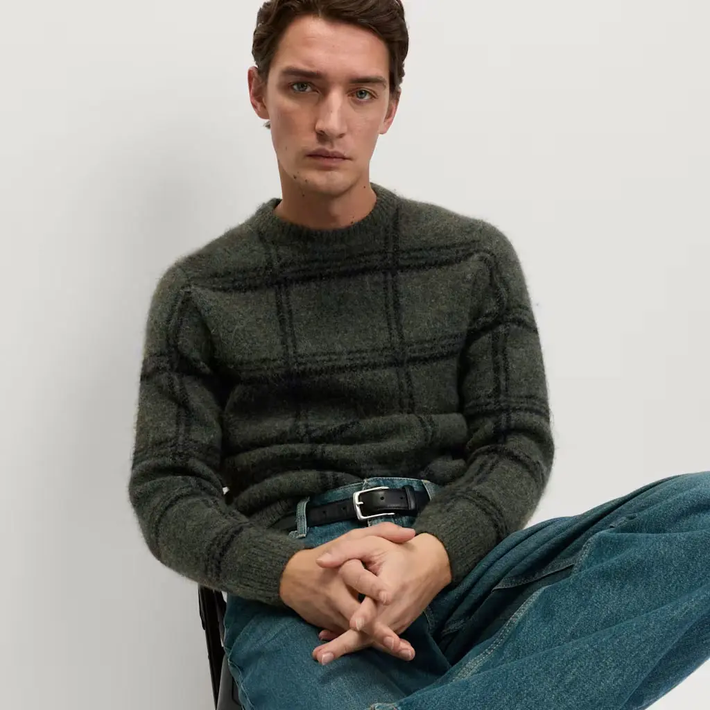 Man in a checked green jumper with blue jeans and a black belt