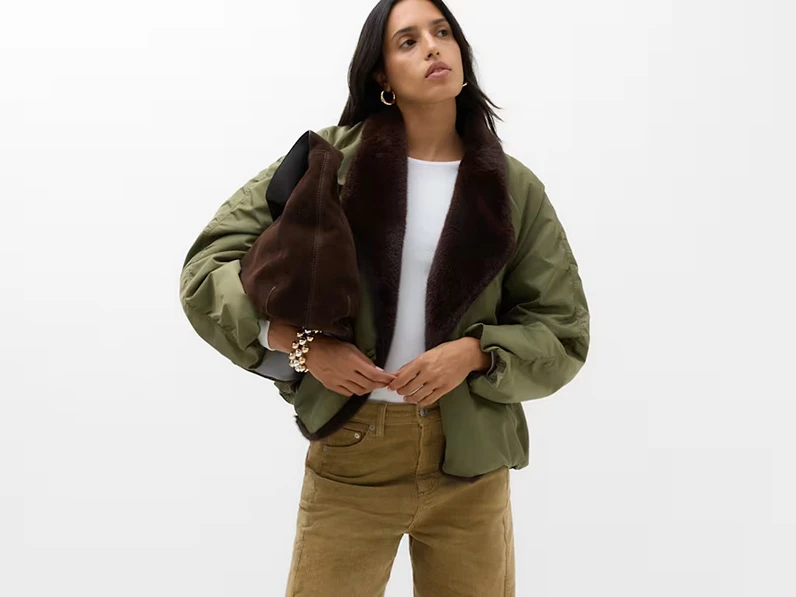 Woman wearing a green satin bomber jacket with a faux fur collar, white T-shirt and beige corduroy trousers.