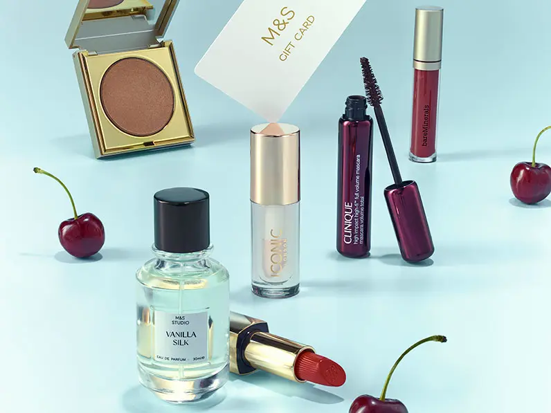 Collection of beauty gifts including perfume, make-up and gift card on a blue background.
