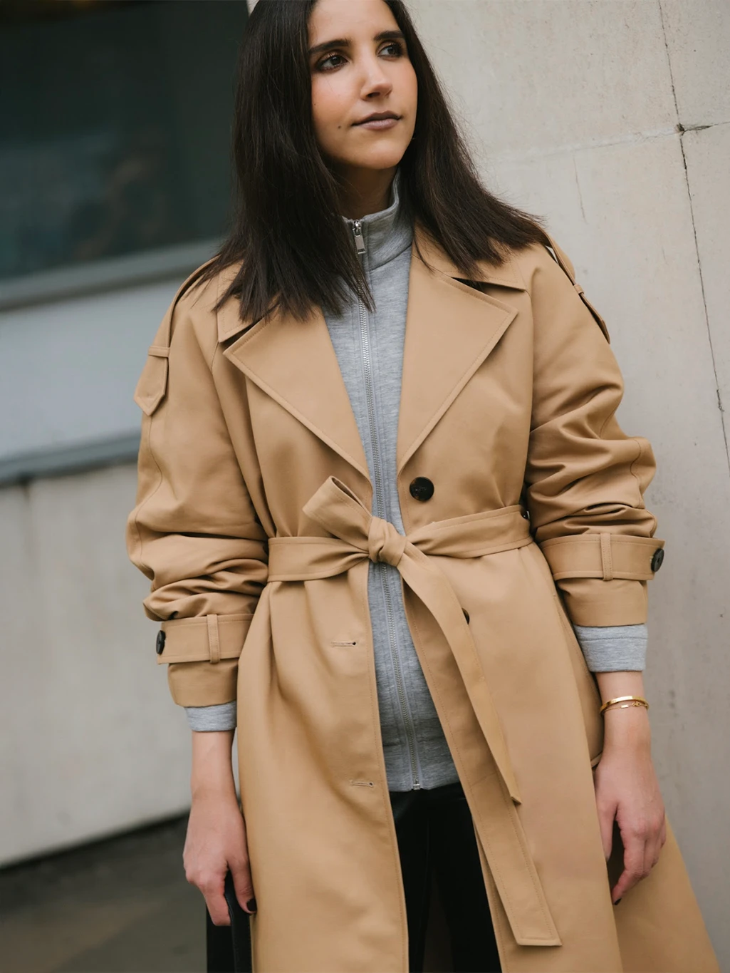 Humaa Hussein wearing a warm beige trench coat with a grey hoodie and black leather trousers