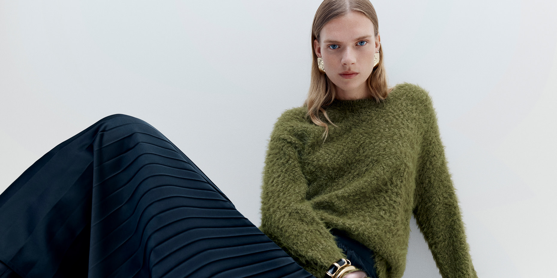 Woman wearing green jumper and black pleated skirt