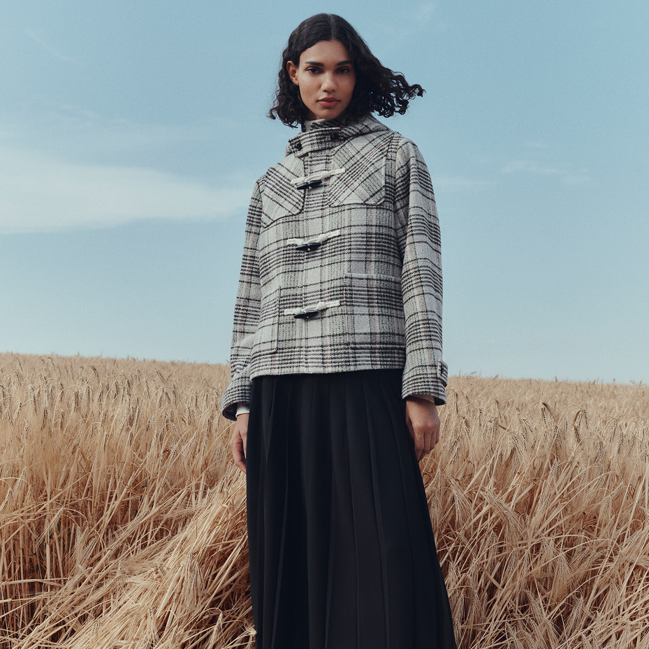 Woman wearing grey checked jacket and black skirt in a field