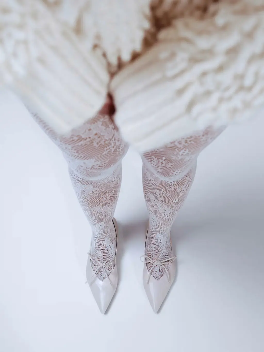 Woman wearing a white jumper with white fishnet tights and white point-toe heels