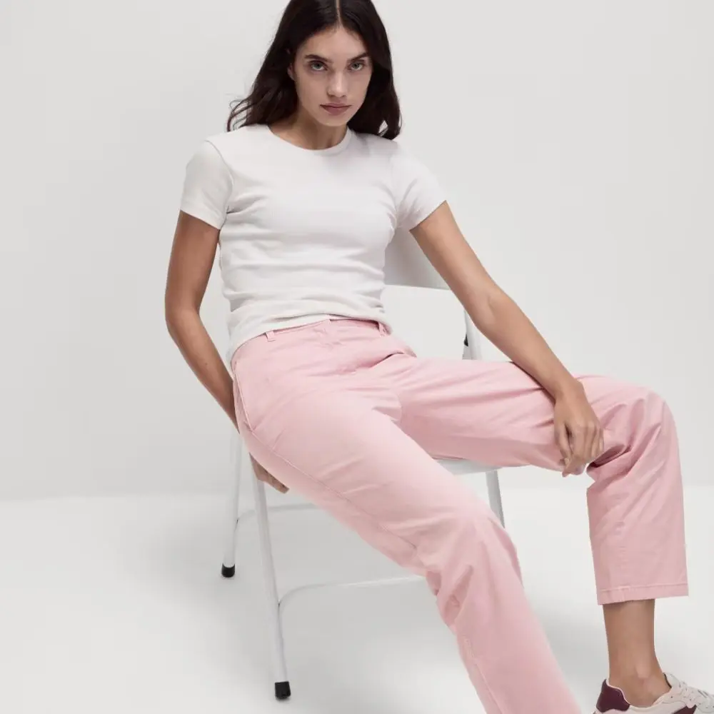 A woman sat on a chair wearing a white t-shirt and pink chinos