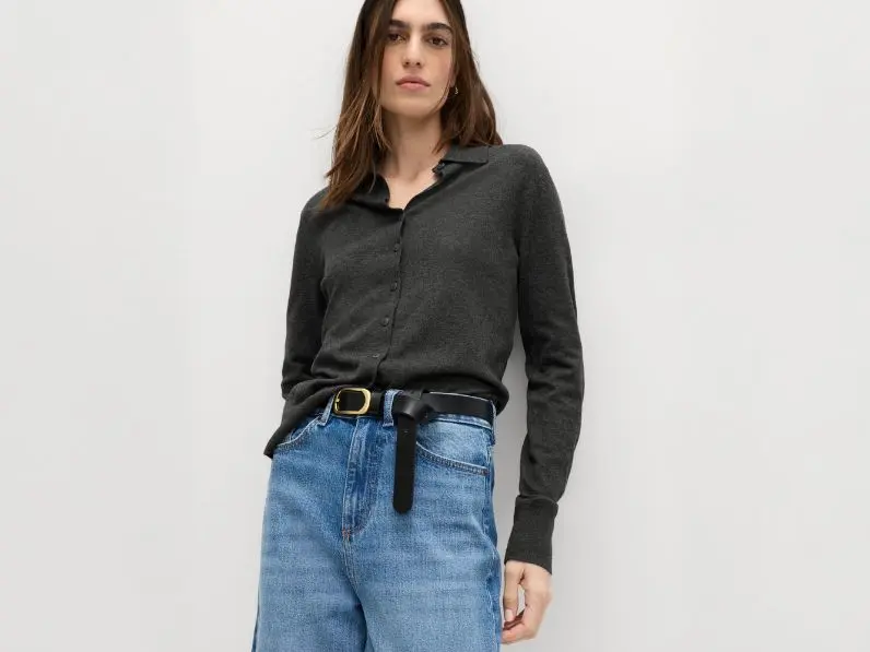 A woman wears pale blue jeans with a grey shirt tucked in and a leather belt